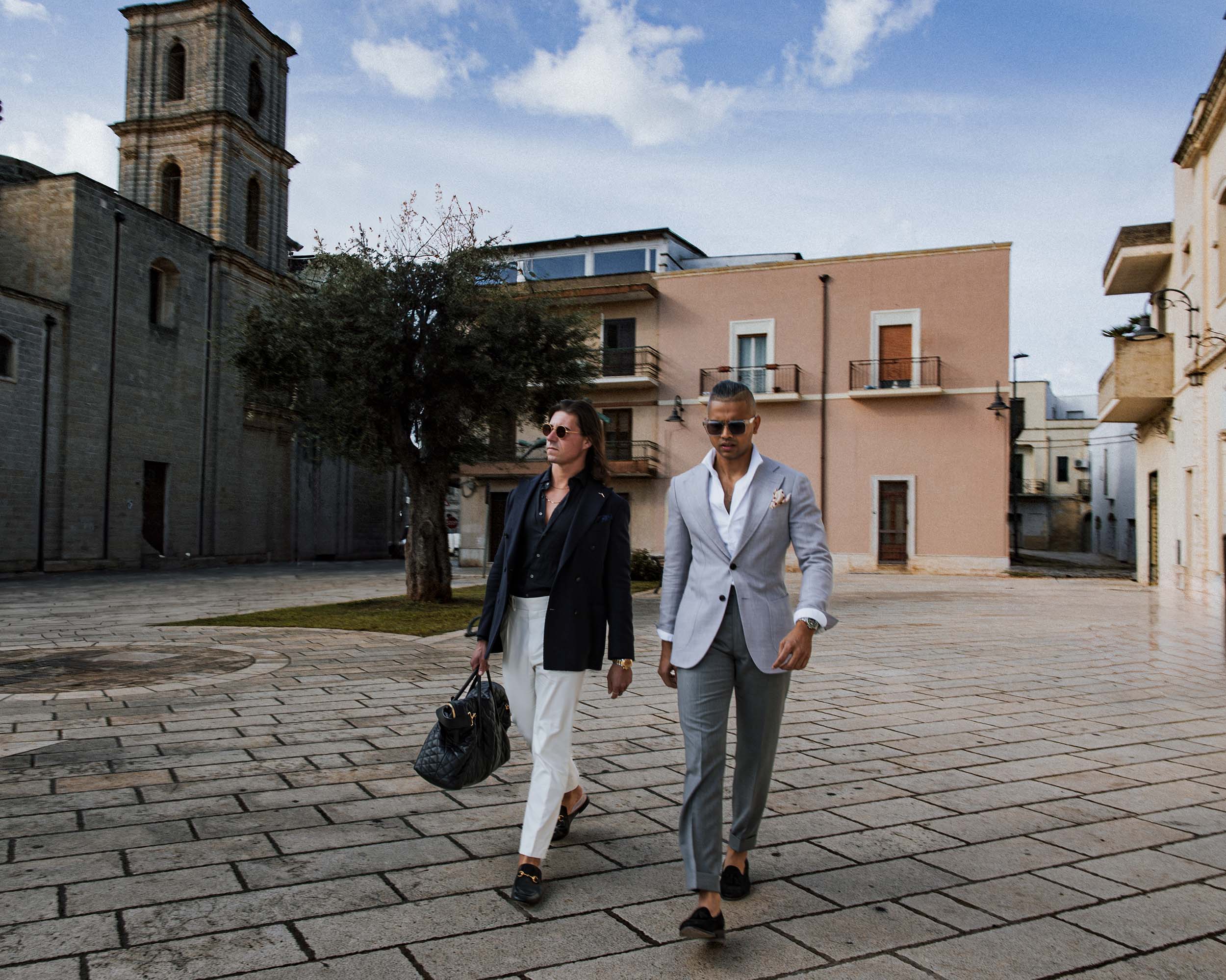 Two Don Marrón members walking through an Italian piazza in tailored suits, embodying refined menswear, confidence, and modern European sophistication.