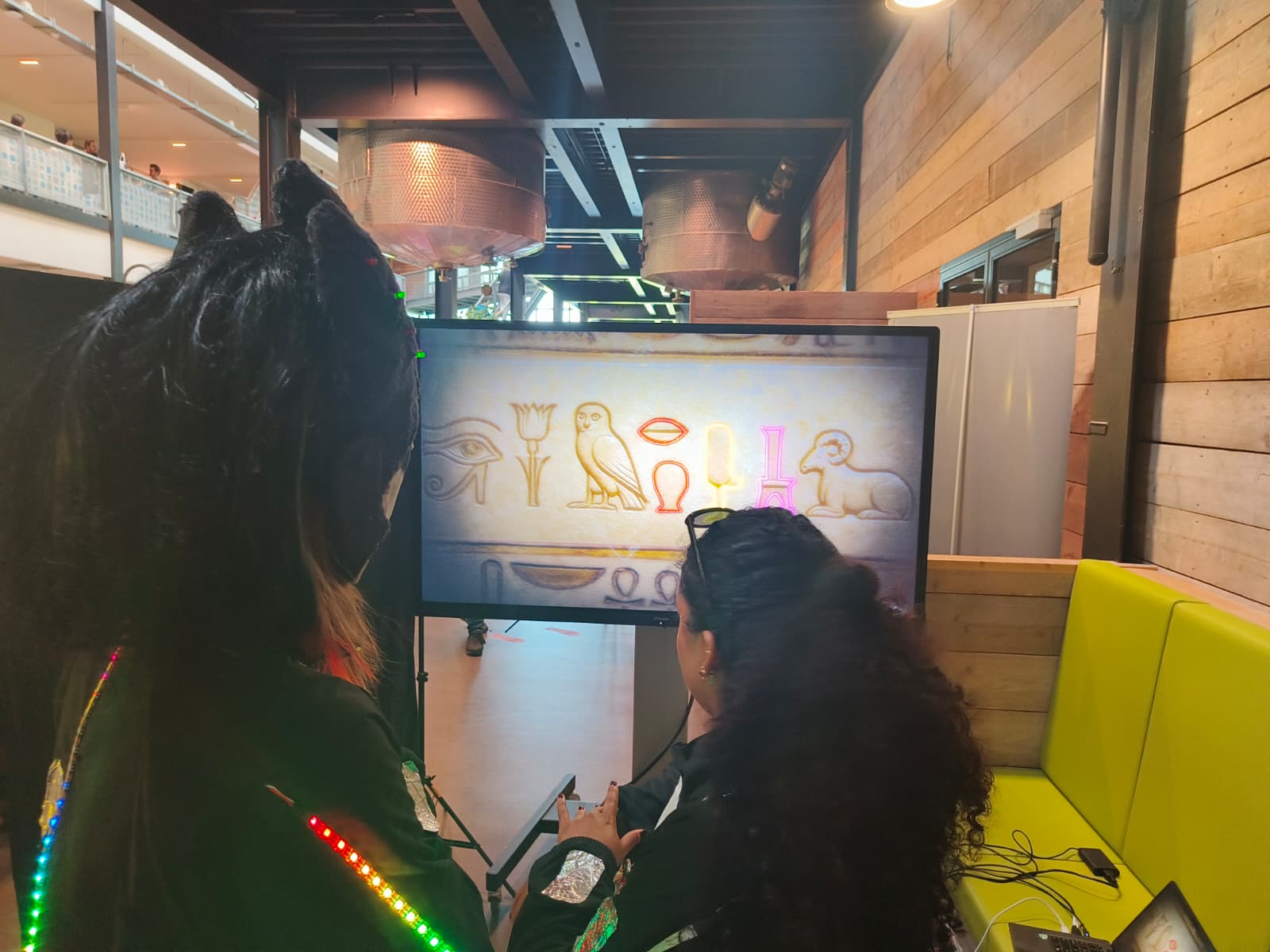Two people lookng at a screen with hieroglyphics wearing neon light jackets