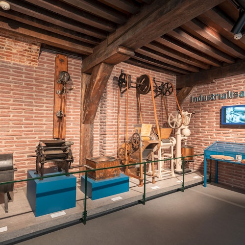 Egy kiállítási vitrin ipari korszakbeli gépekkel és szerszámokkal egy téglafal előtt, amelyen az "Iparosodás" felirat található.
