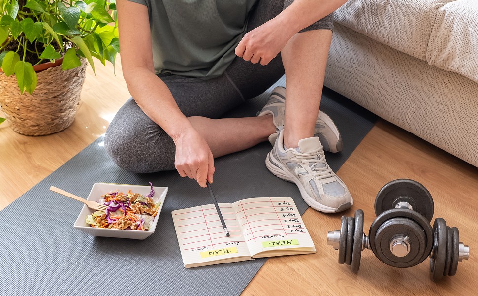 Person sitting down on a yoga mat with a salad and bumbells