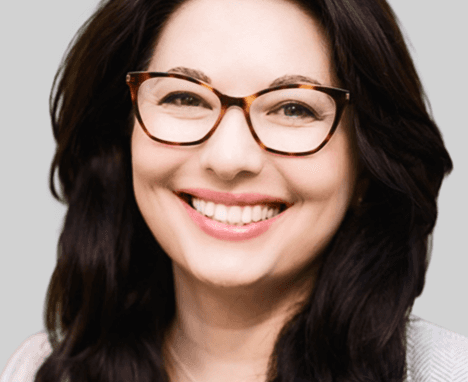 Smiling blonde woman with freckles in a white shirt, arms crossed, minimalist studio portrait.