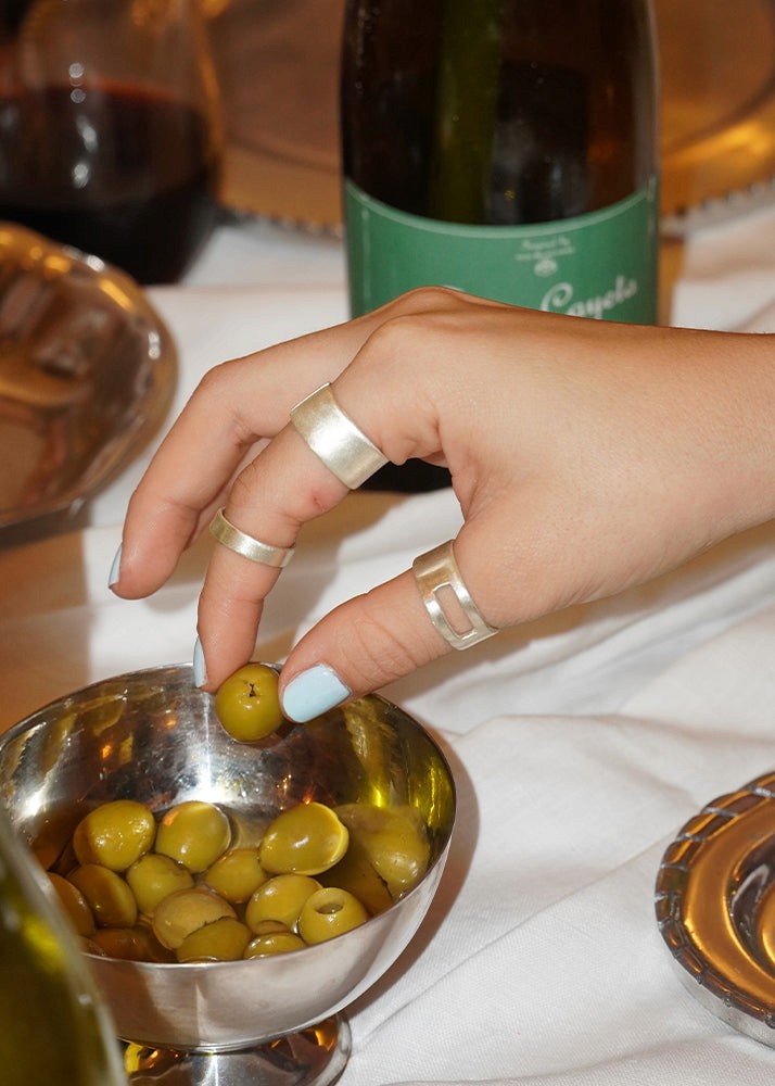 Hand picking a green olive from a bowl with a bottle of wine in the background