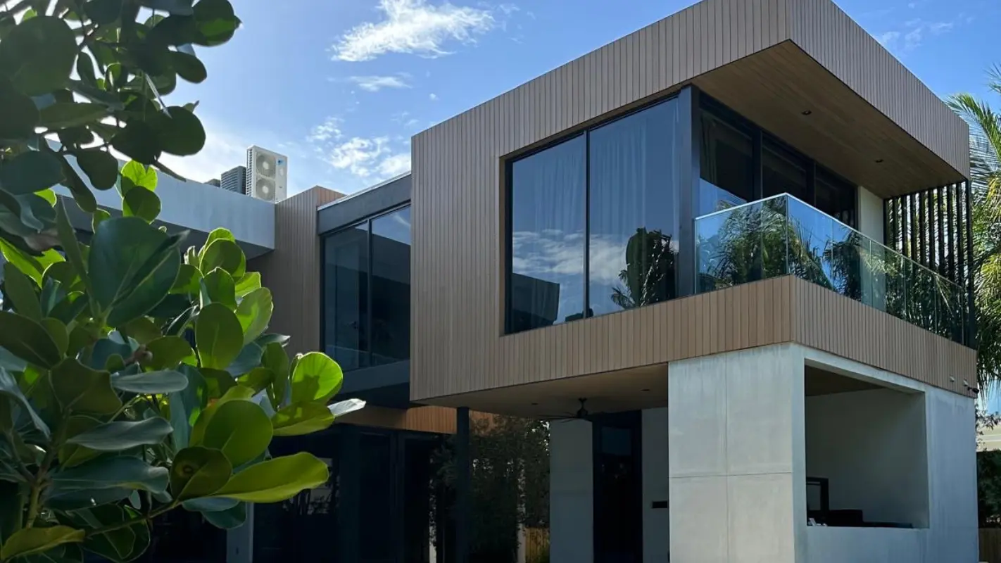 Side exterior of Meridian Avenue Residence in South Beach — wood-clad cantilevered upper level with glass-railed balcony and concrete base, surrounded by tropical landscaping, by Atelier International.