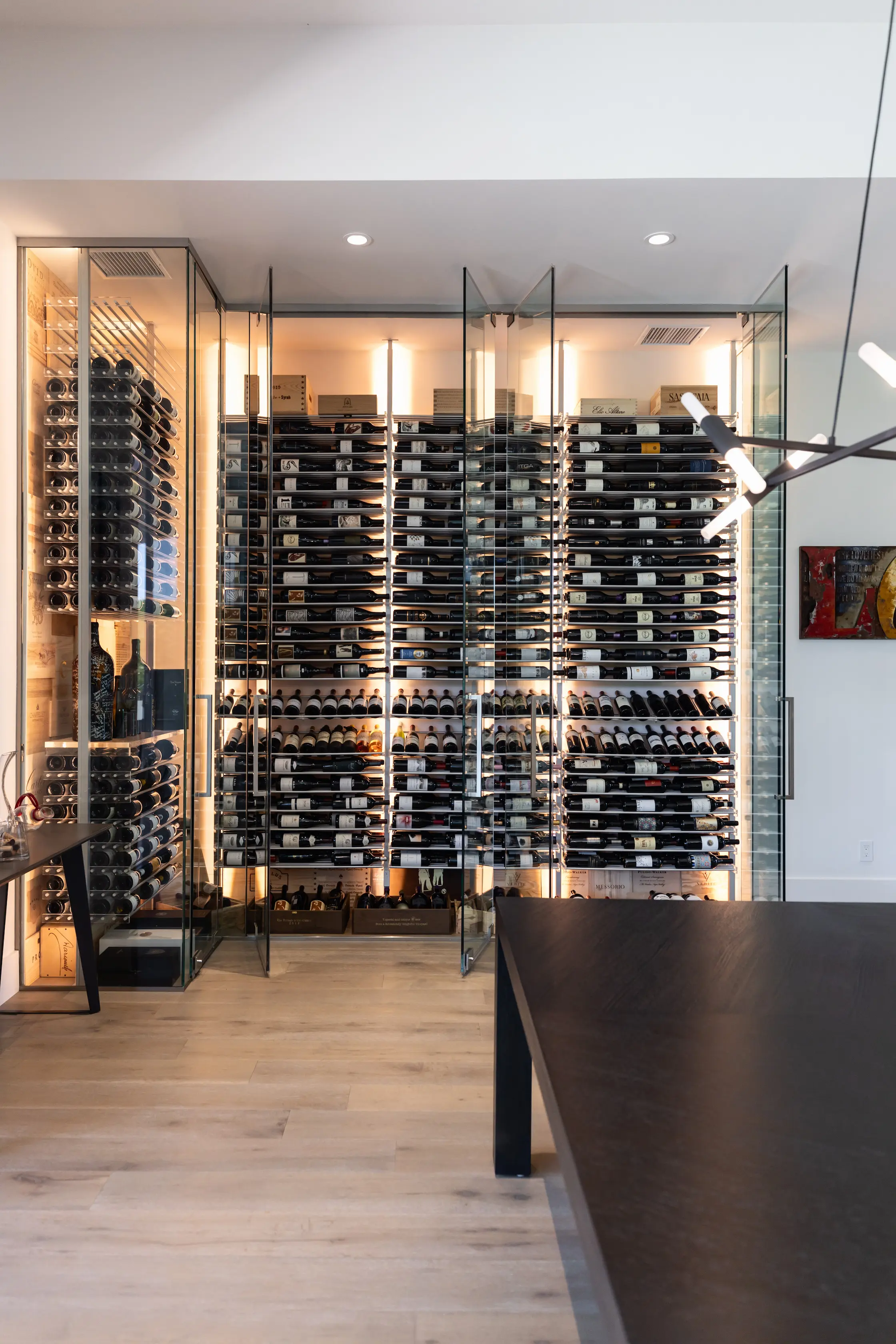 Modern custom wine cellar with label-forward wine racking displaying standard bottles, magnums, and Champagne; climate-controlled glass wine wall designed by Innovative Wine Cellar Designs for luxury home collectors.