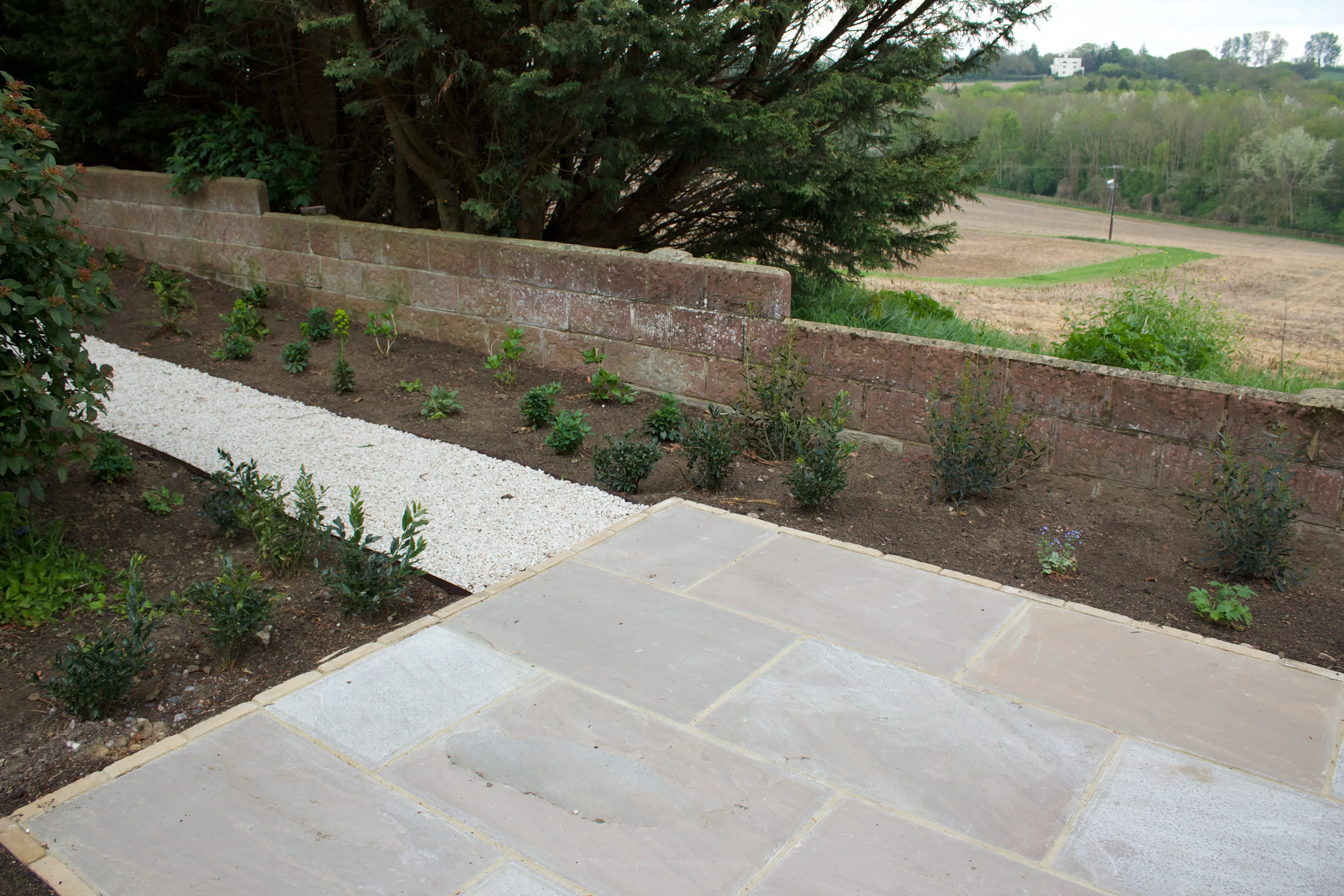 A stone pathway leads through a garden, with grassy fields in the background under a cloudy sky.
