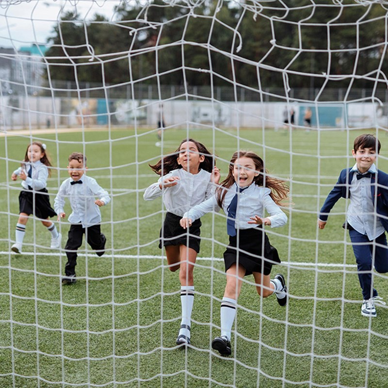 Photo of children playing football with the shot taken through the net of a football gaol