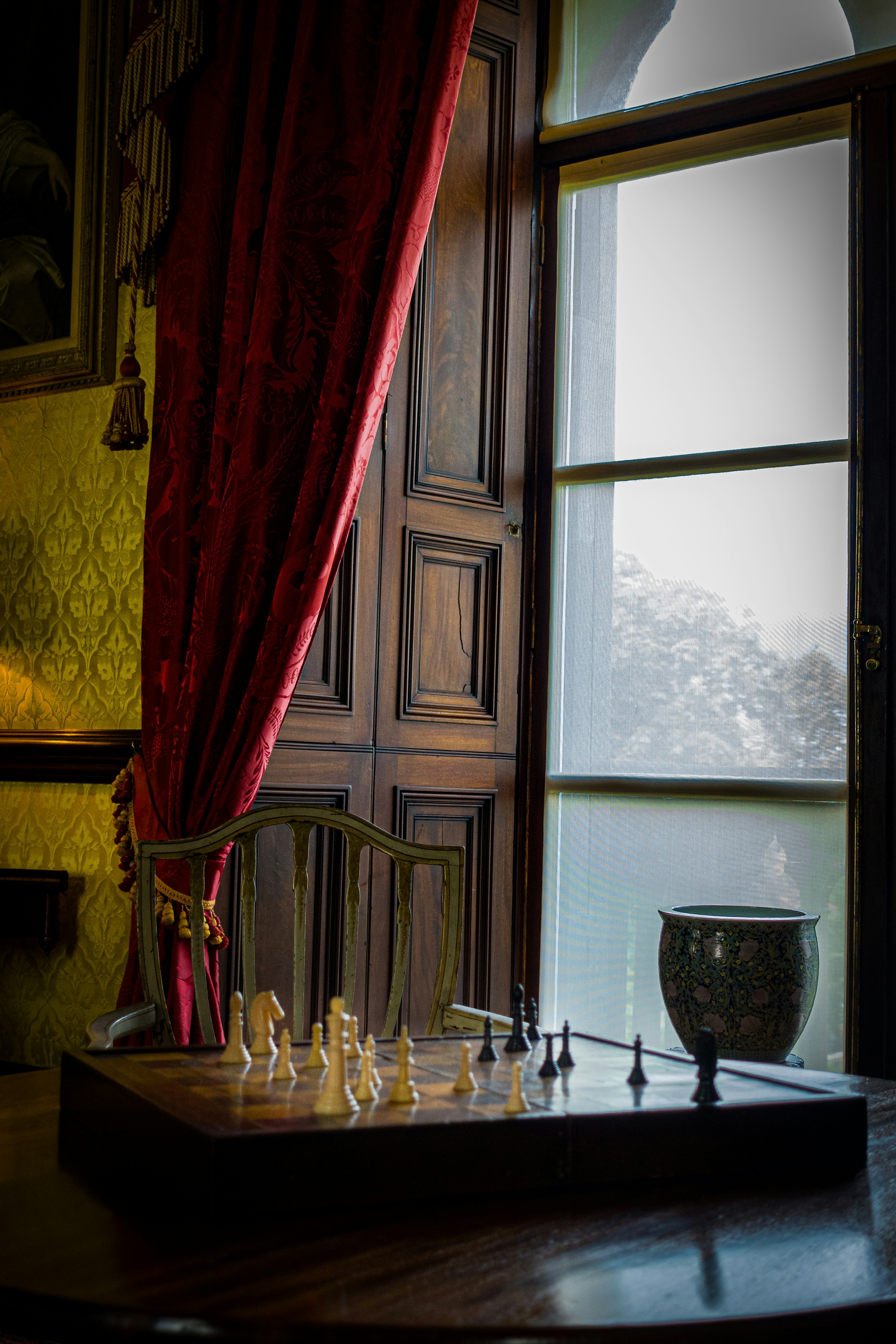 An open window beside a table with a chess set placed on it.