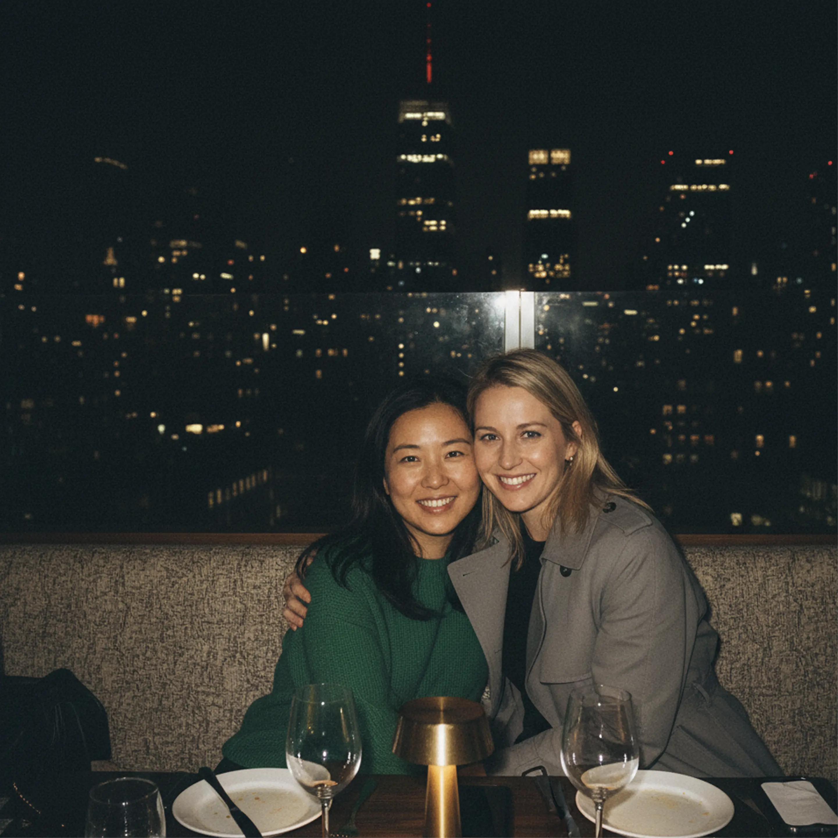 Wooden outdoor table set with multiple plates of food, including dips, salads, potatoes with cheese, and glasses of water, with hands reaching in to eat.
