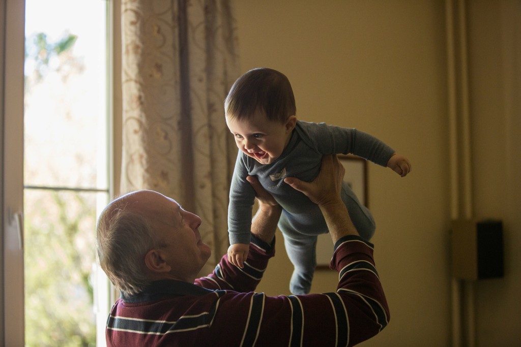 Grandfather holding his baby grandson in his arms, both laughing and creating unforgettable memories.