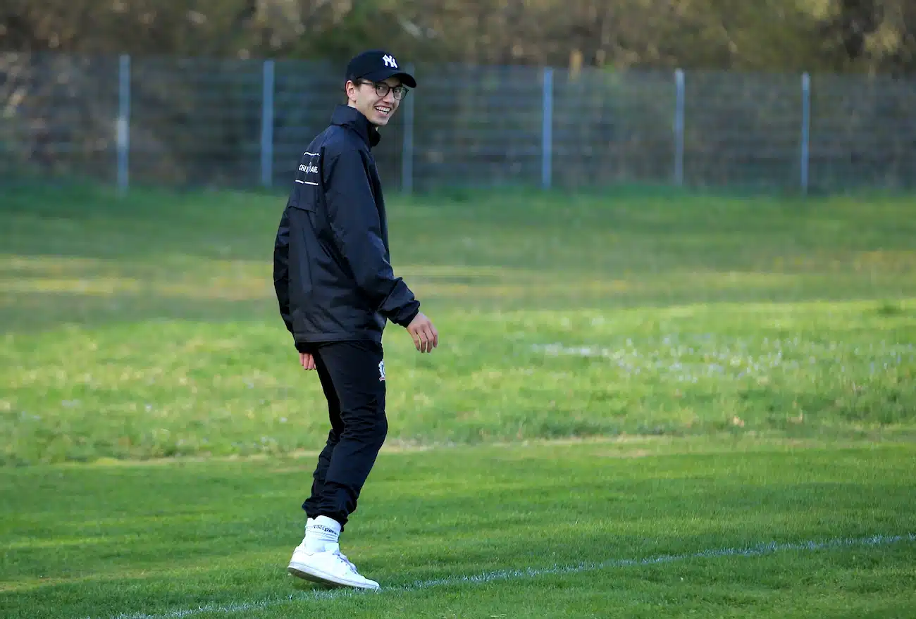 Our founder Thiago as a young football coach walking across a lush green field, smiling confidently. This image accompanies the story of CoachingArea's origins, highlighting the founder's journey from managing time-consuming tasks as a coach to creating an innovative platform that simplifies organisational challenges in amateur and youth sports.