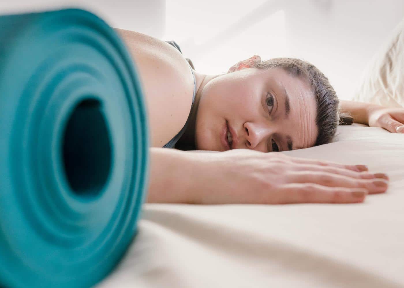 Woman laying on bed with yoga mat by her side
