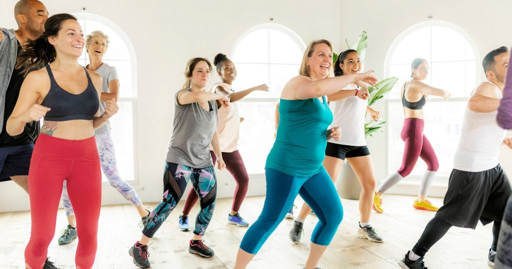 A diverse group of people energetically participating in a dance fitness class in a bright studio.