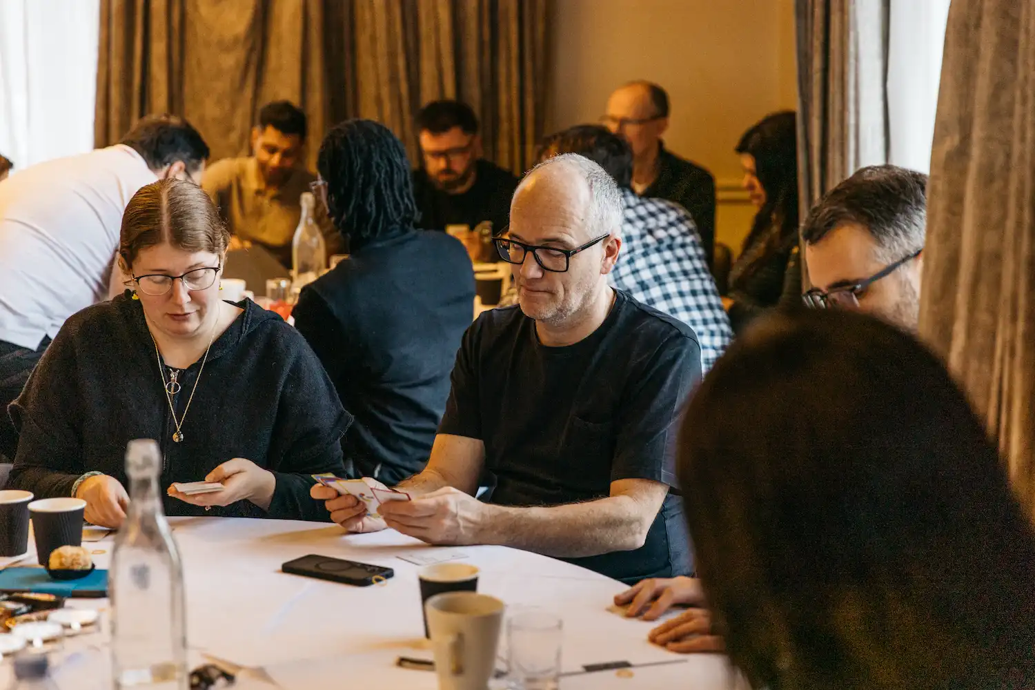 People sitting at a table with some phones and cups.