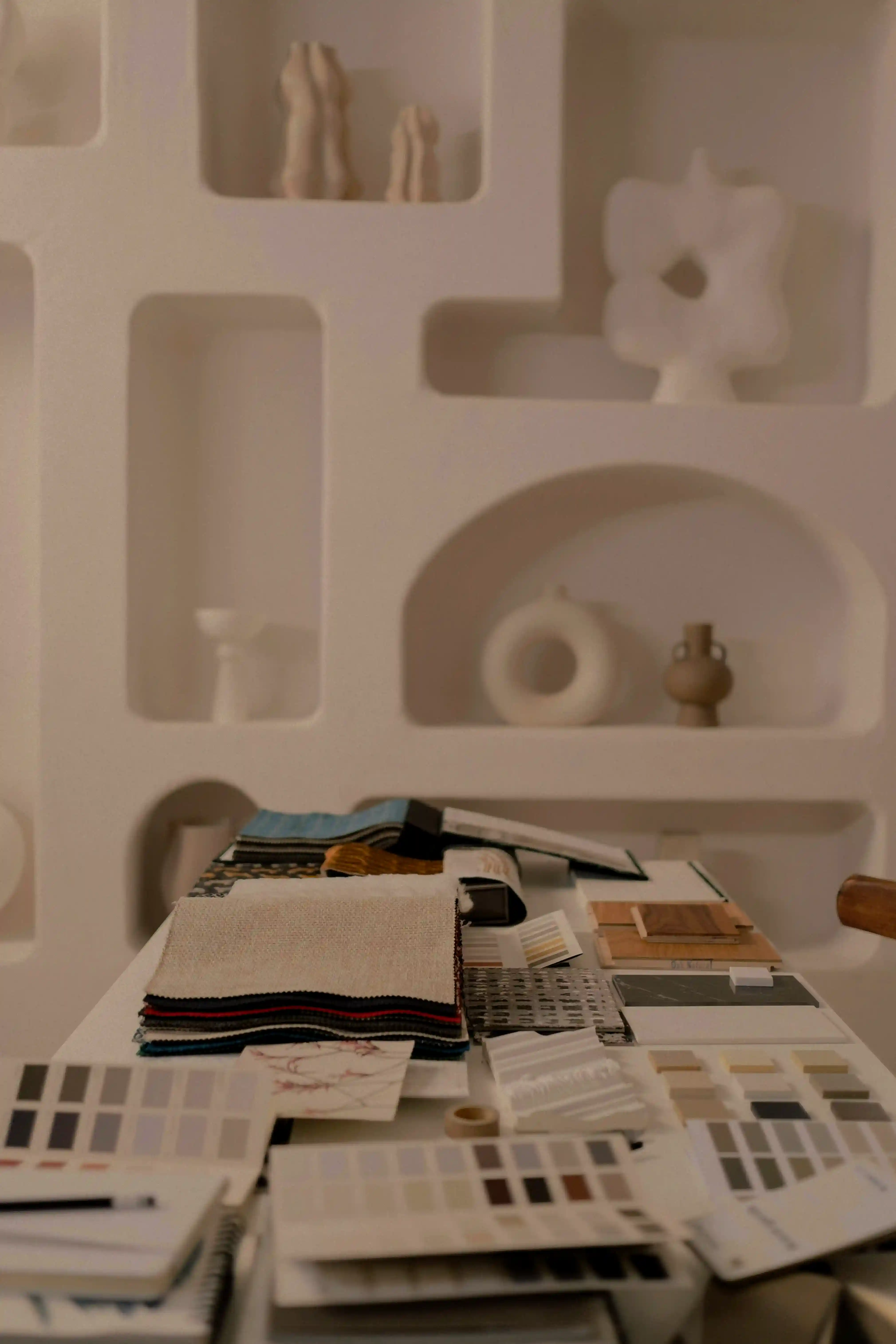 A scene of a table filled with swatch books overlooking a shelf filled with ceramic vases