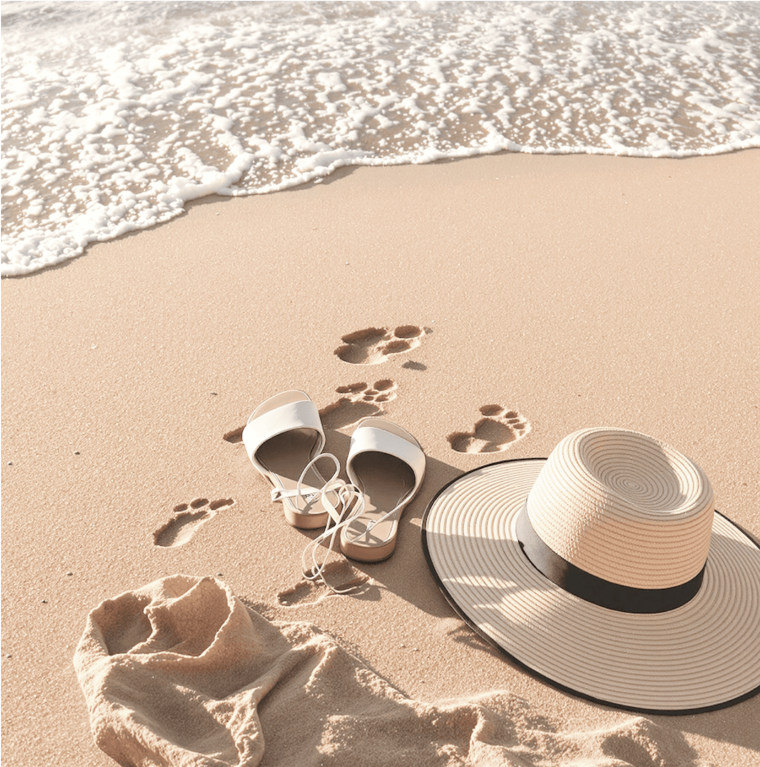 Hat, sandals, and footprints on sandy beach with gentle ocean waves