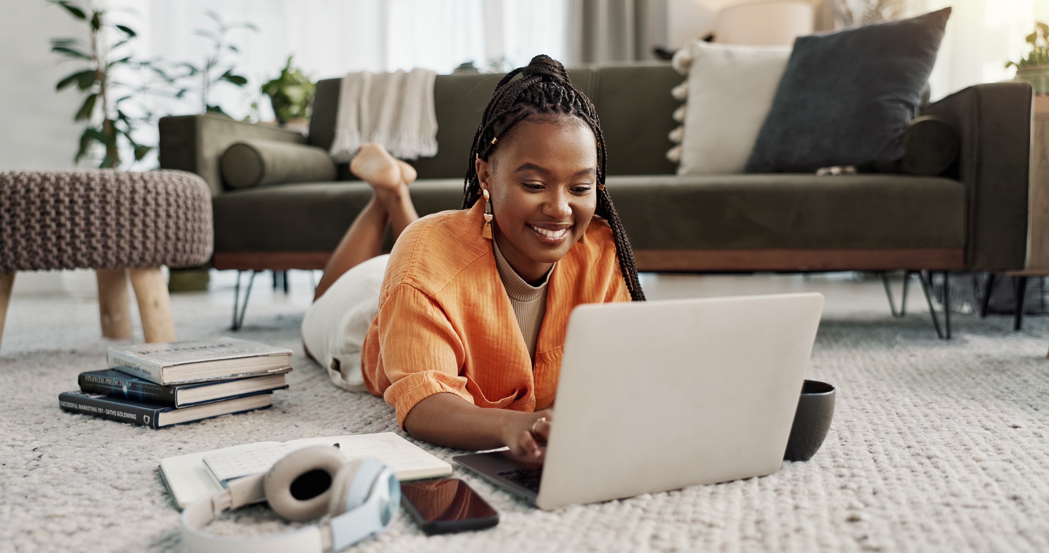 Young woman relaxing on the floor with a laptop, headphones, and books at home