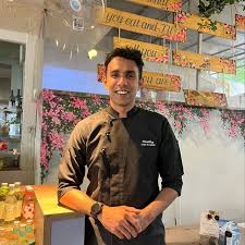 A young woman with long hair smiles while standing against a green backdrop, wearing a casual dark sweater.