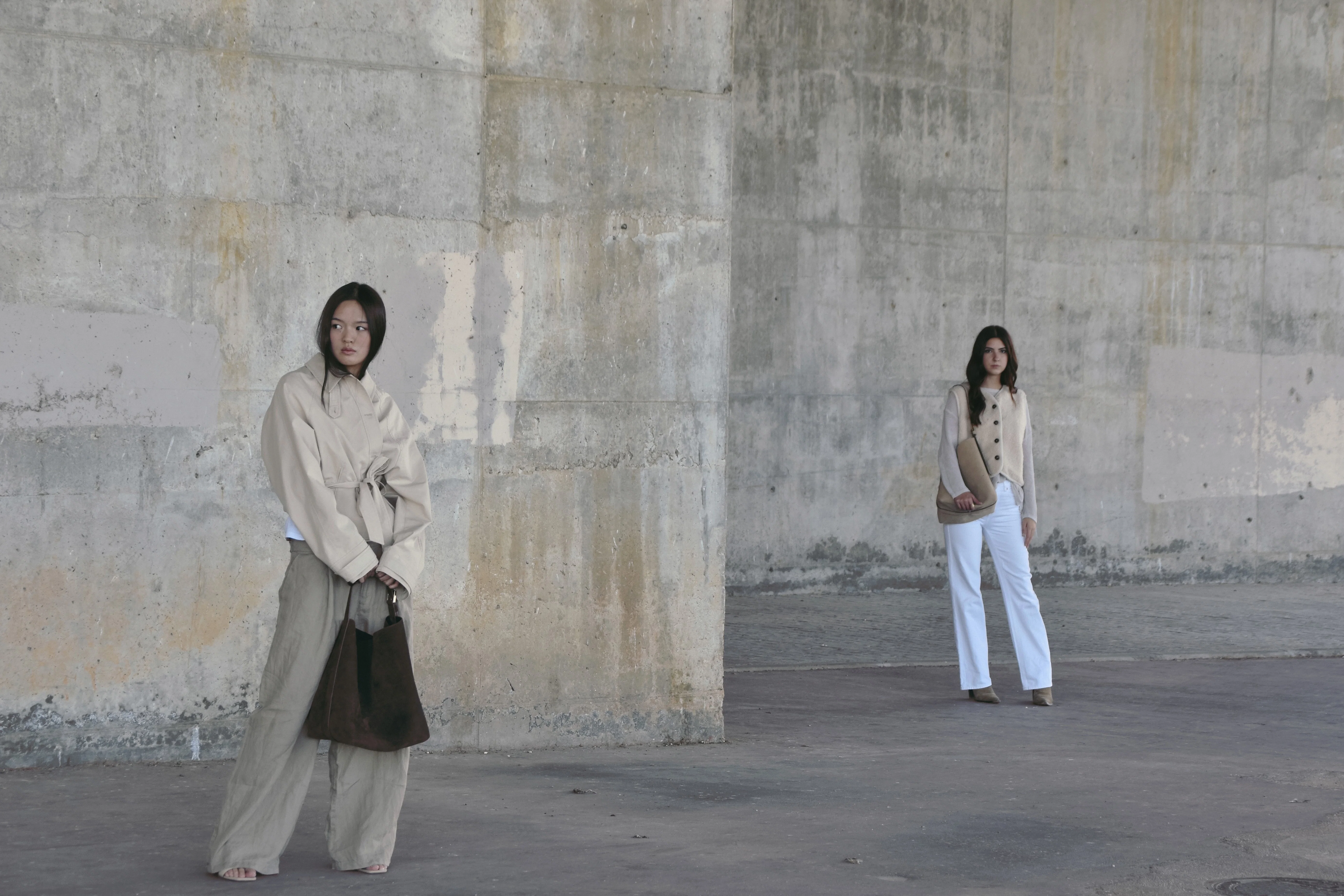 Modelos posando en una pared brutalista con bolsos de la marca de bolsos artesanales Lulia Spain