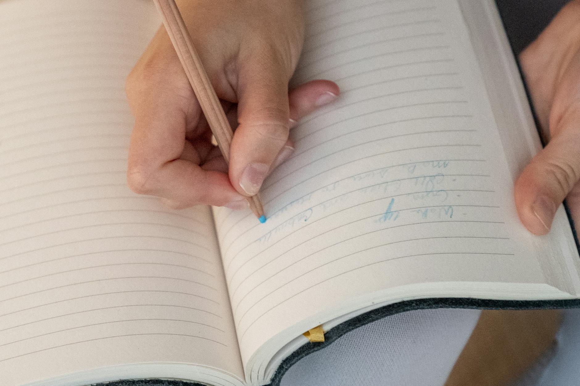 A close-up of a teacher's hand writing a psychomotor learning objective on a whiteboard with a blue marker.