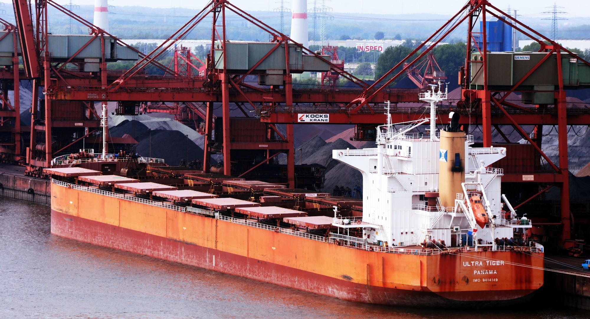 M/V ULTRA TIGER (IMO 9414149) alongside a bulk terminal with shiploader cranes — bulk carrier at berth prior to cargo operations and cargo hold preparation (coal to grain standards).