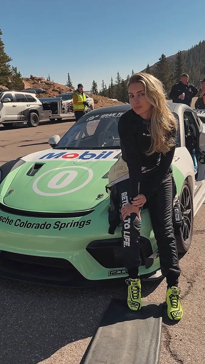 Emelia Hartford stands next to a bright green Porsche sports car with a Mobil 1 decal across the hood on a sunny day.