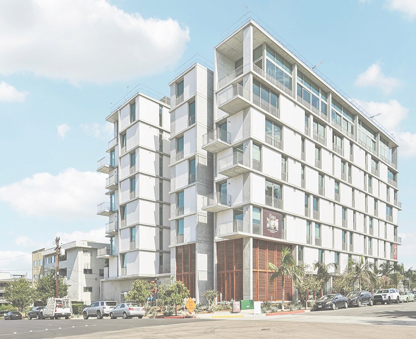 Modern apartment building with white, modular facade and large windows, set against a blue sky.
