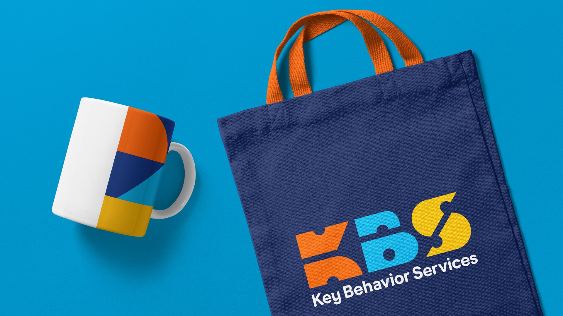 Coffee mug and tote bag one light blue background with colorful KBS branding.