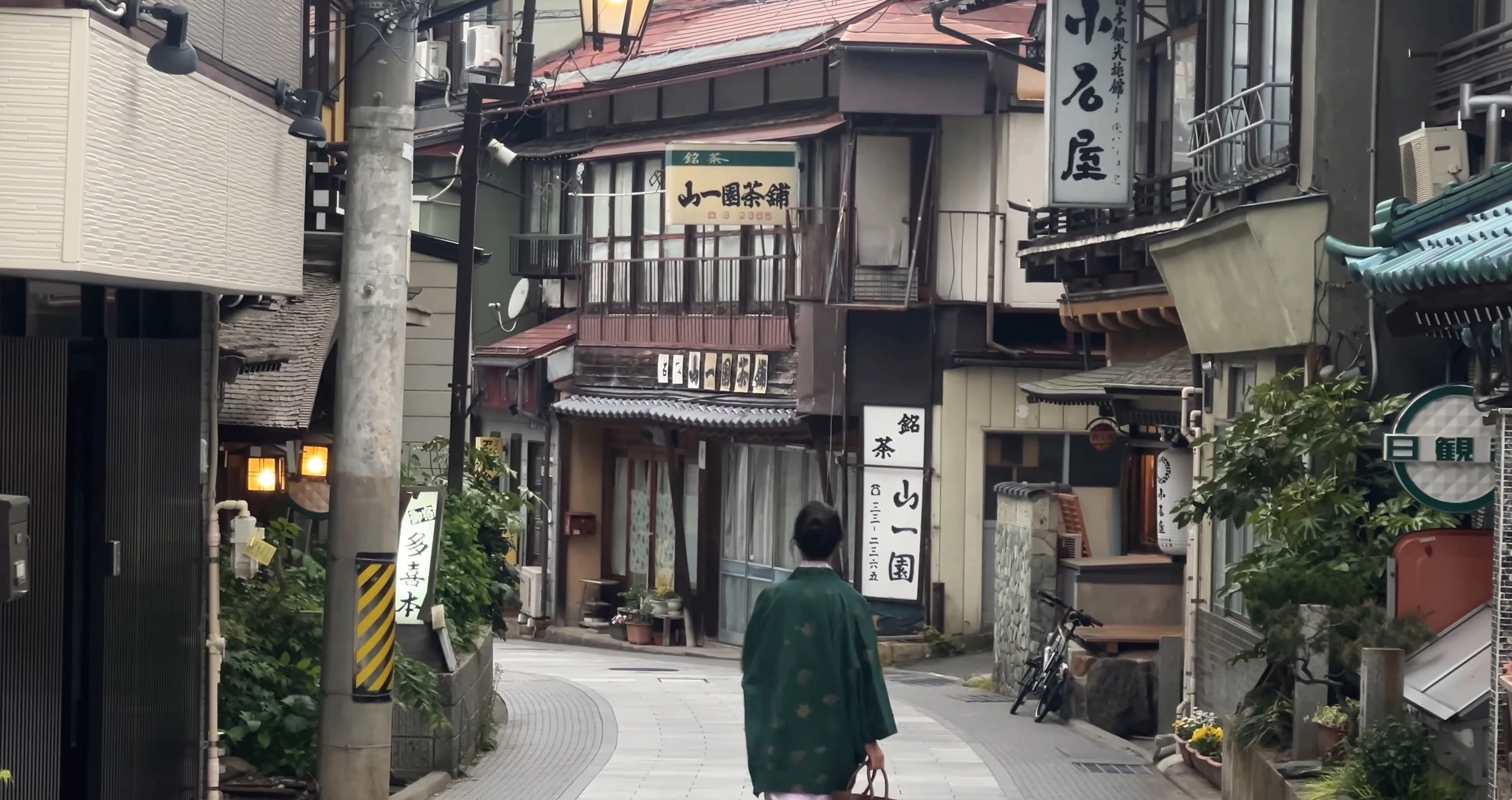 A guest in a green yukata walks through the historic stone-paved alley of Shibu Onsen at dusk