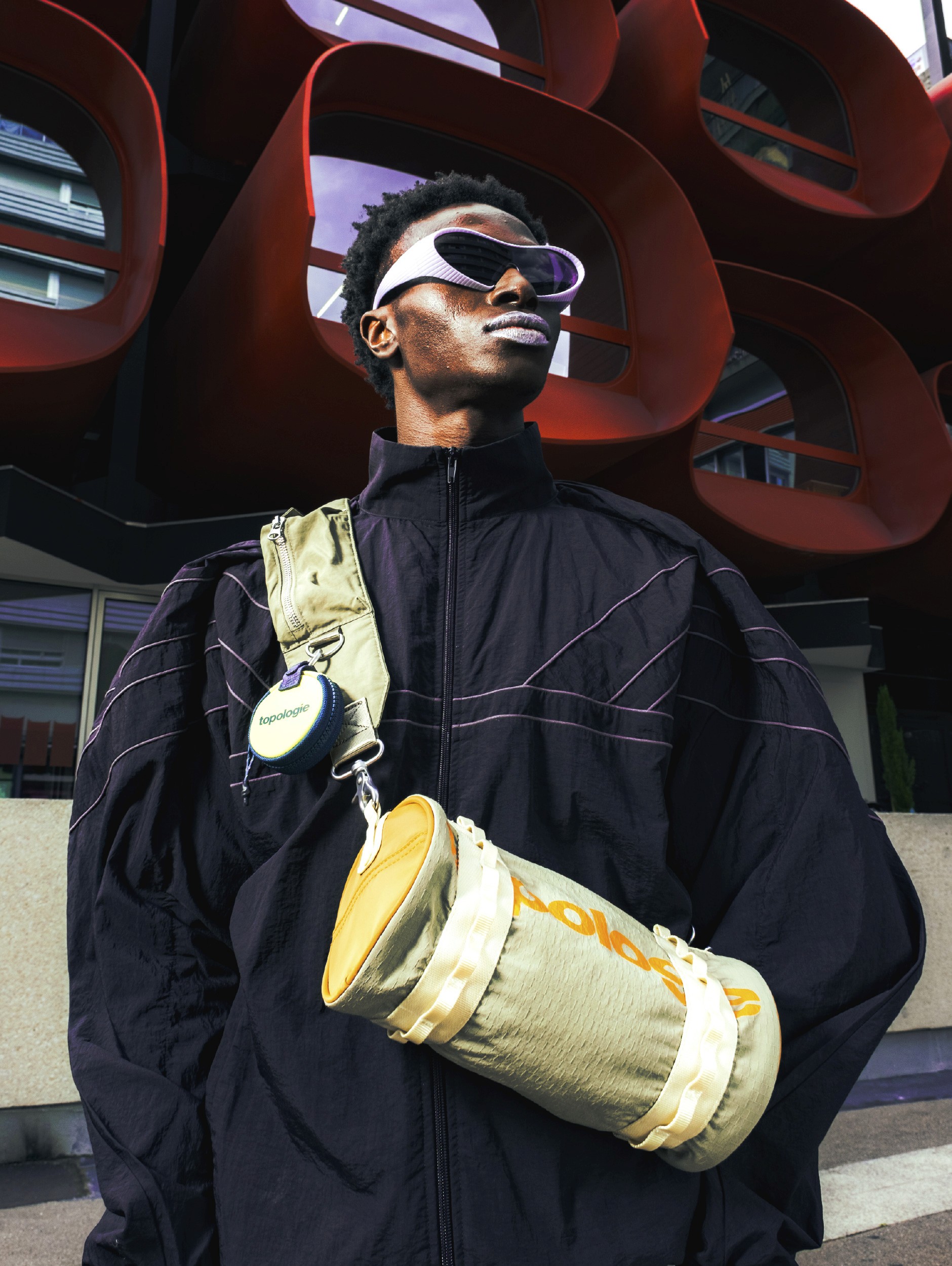 Homme portant une sacpche beige de la marque apparente Topologie devant un immeuble 70's space-age