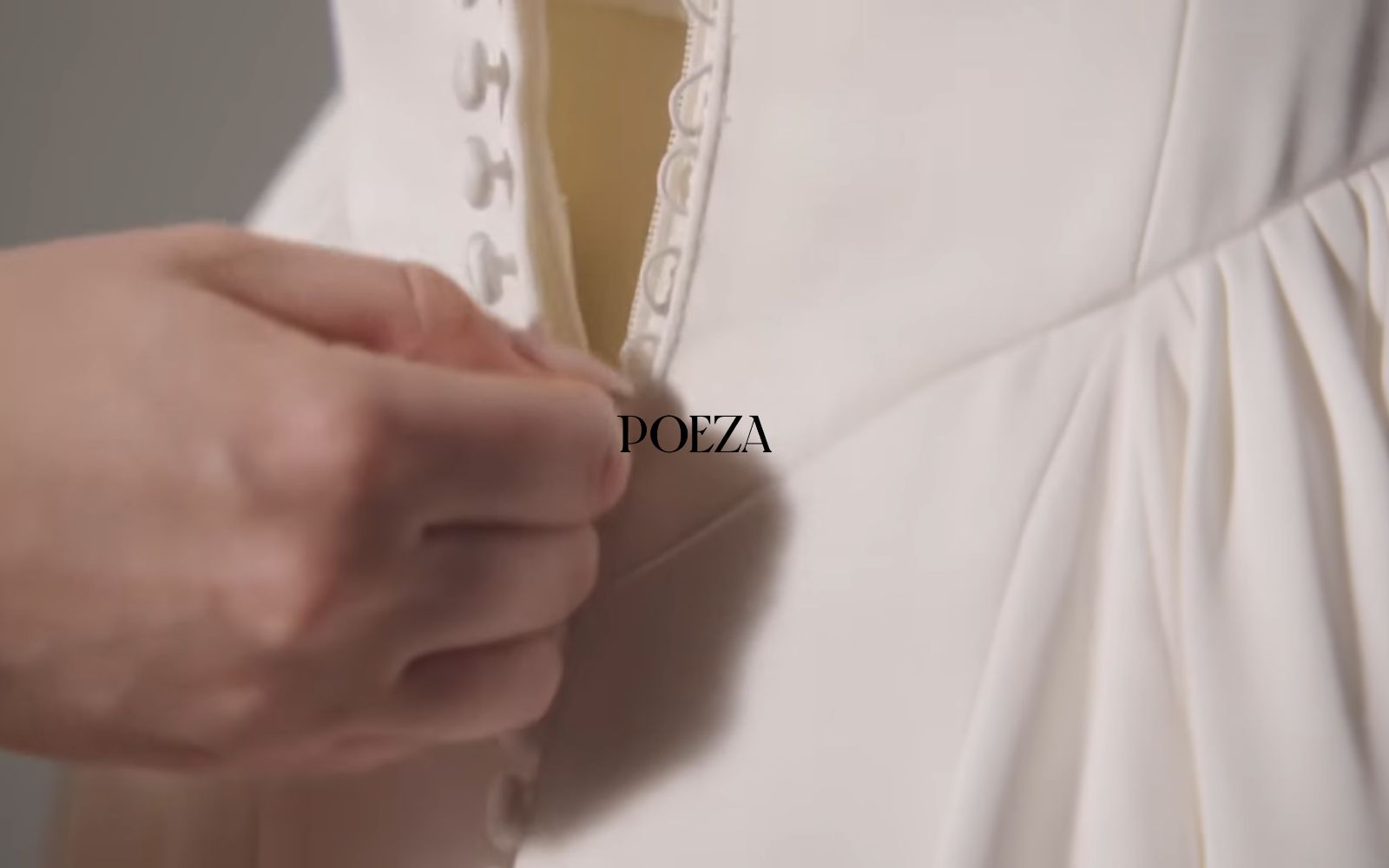 Close-up of a hand buttoning a white garment with "POEZA" text overlay.