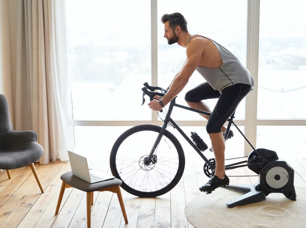 man doing exercise at home while following a workout on his laptop, showing how long to ride stationary bike for weight loss