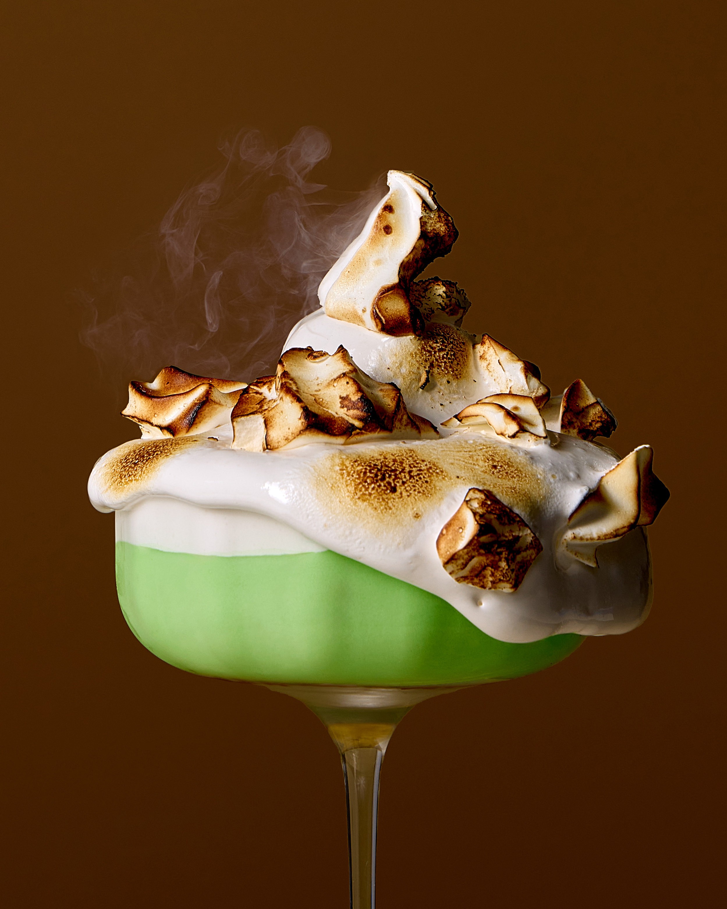 Close view of toasted meringue and smoke above a green dessert coupe