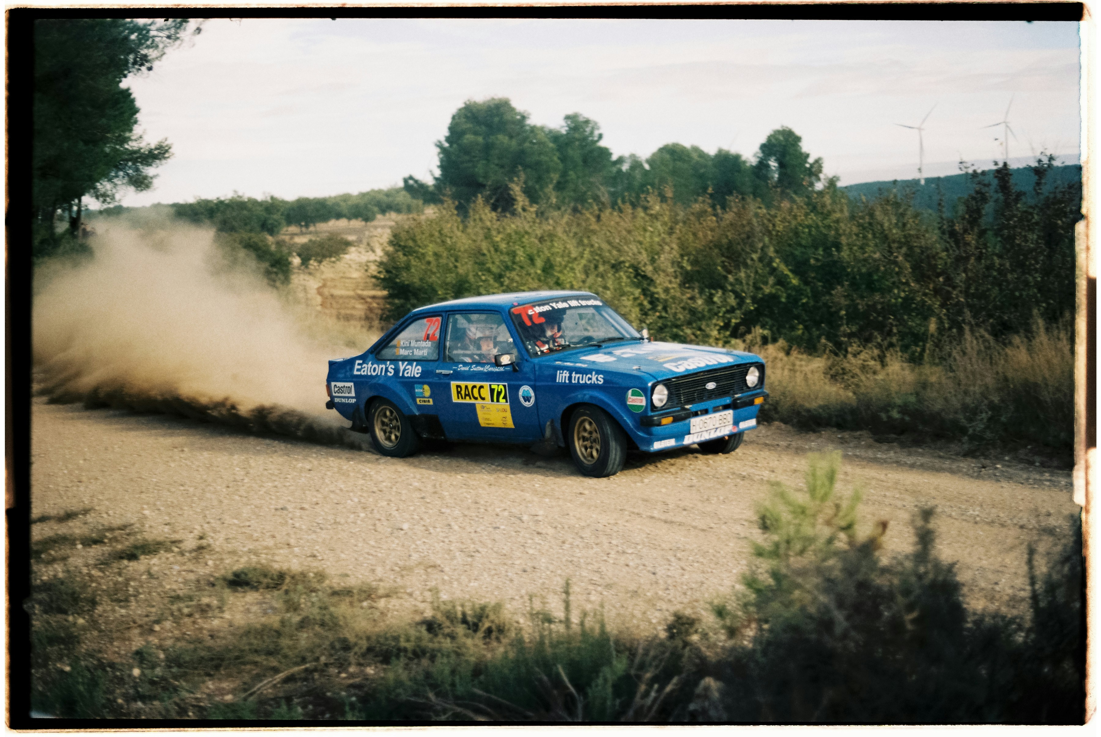 Blue rally car kicking up dust on dirt road