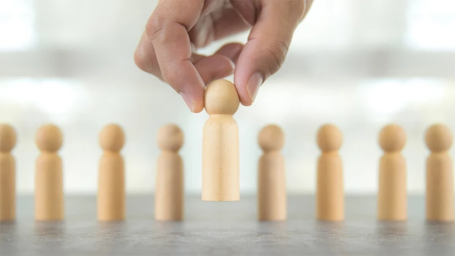 Hand picking up a wooden figure from a row of identical figures, symbolizing leadership or selection.