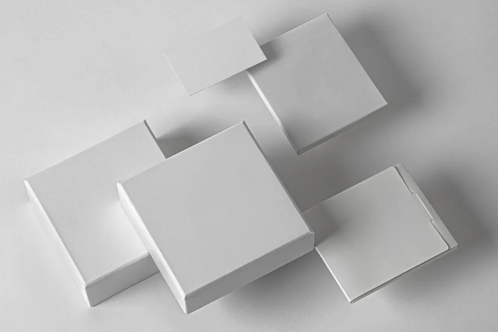 Product packaging mockup set featuring black and white square boxes labeled 0.1, 0.2, and 0.3, along with a business card and manual packaging. Displayed on a dark gray surface with a clean, minimalist layout.