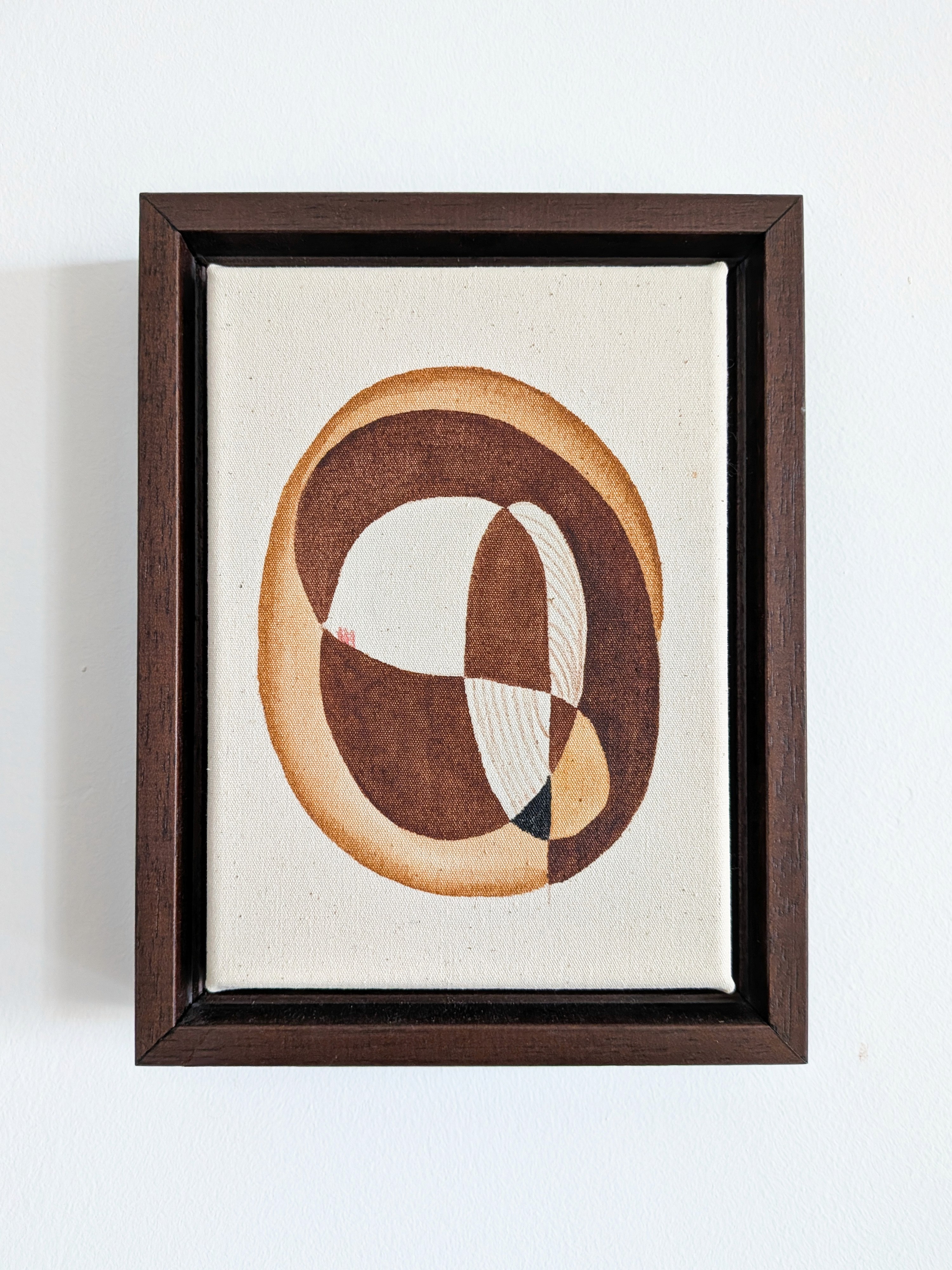 Abstract artwork featuring earthy tones, framed in a dark brown frame against a white wall.
