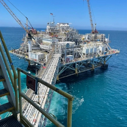 An oil rig in the ocean, with a walkway, cranes, and multiple levels. American flag on top.