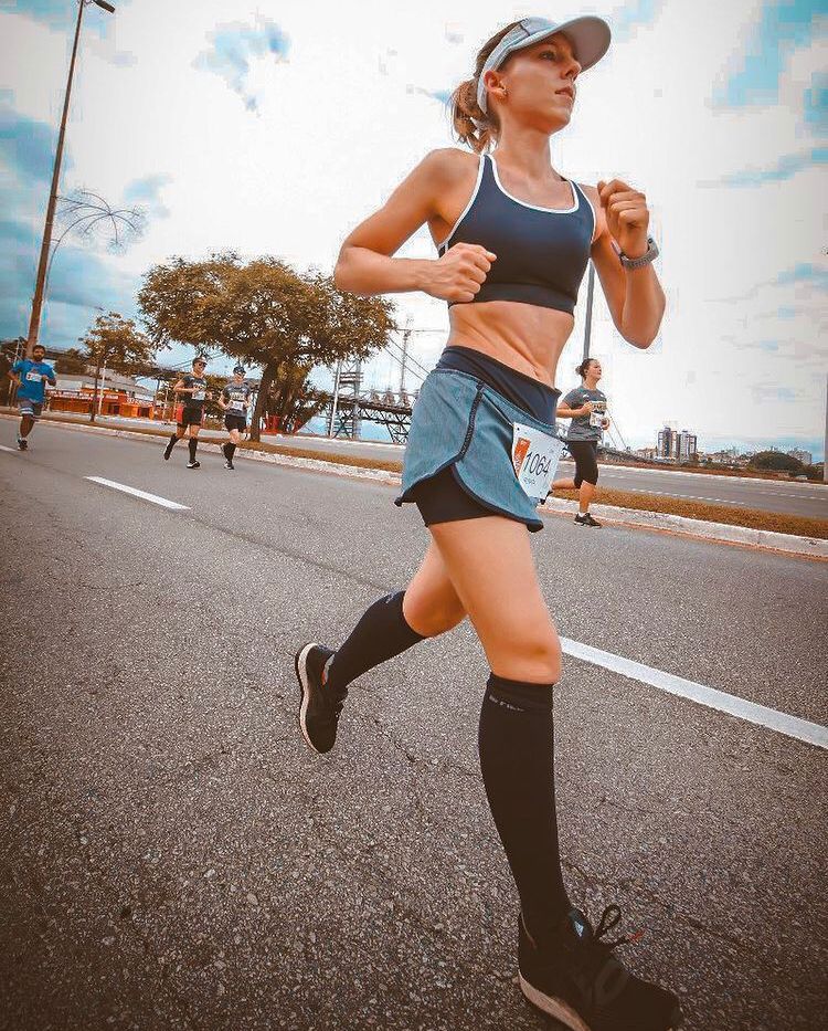 A dimly lit gym scene featuring a barbell rack and weights on the floor, with large windows in the background.