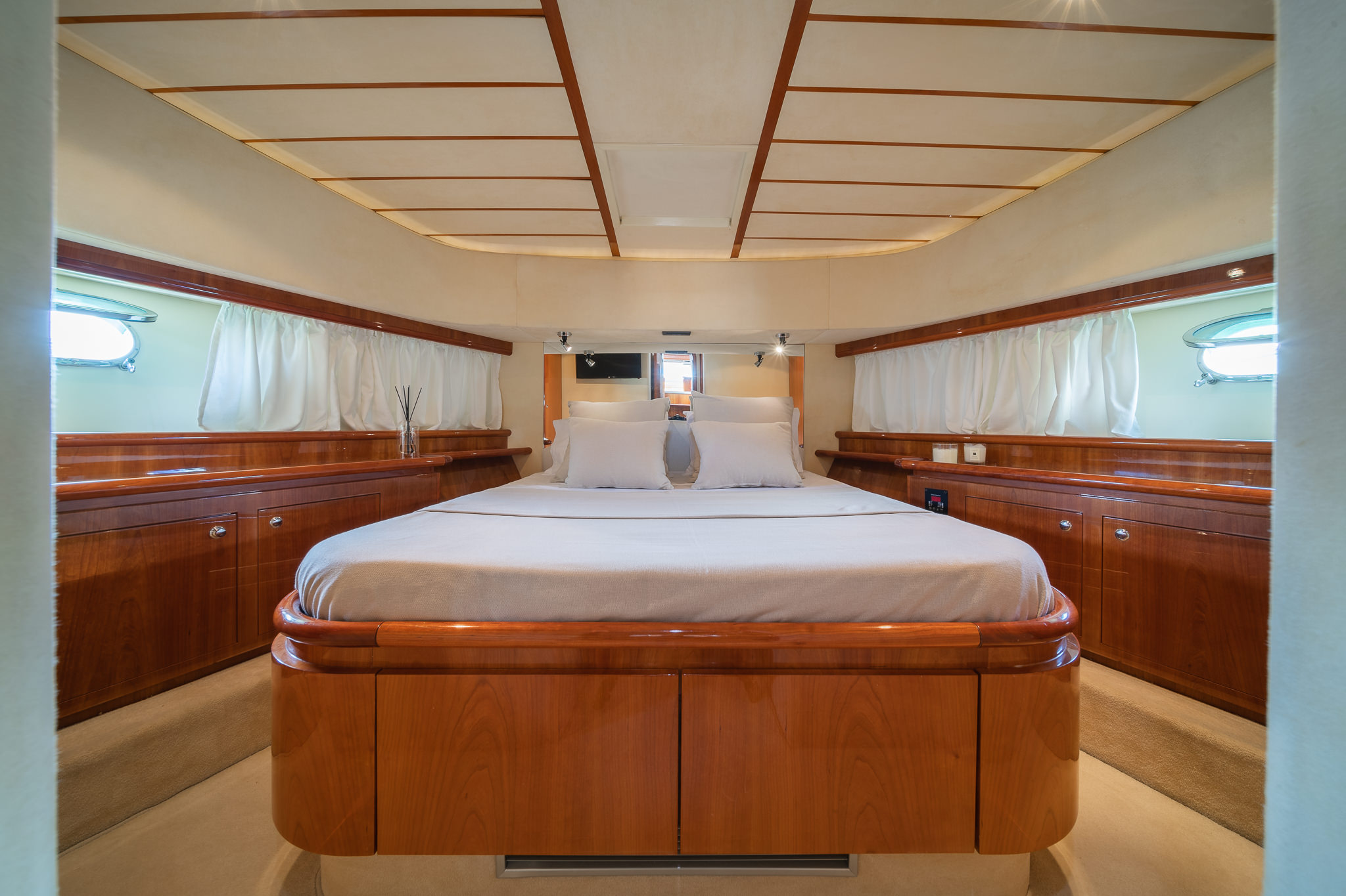 Luxurious yacht cabin interior with polished wood furnishings, double bed, and oval porthole window with natural light.