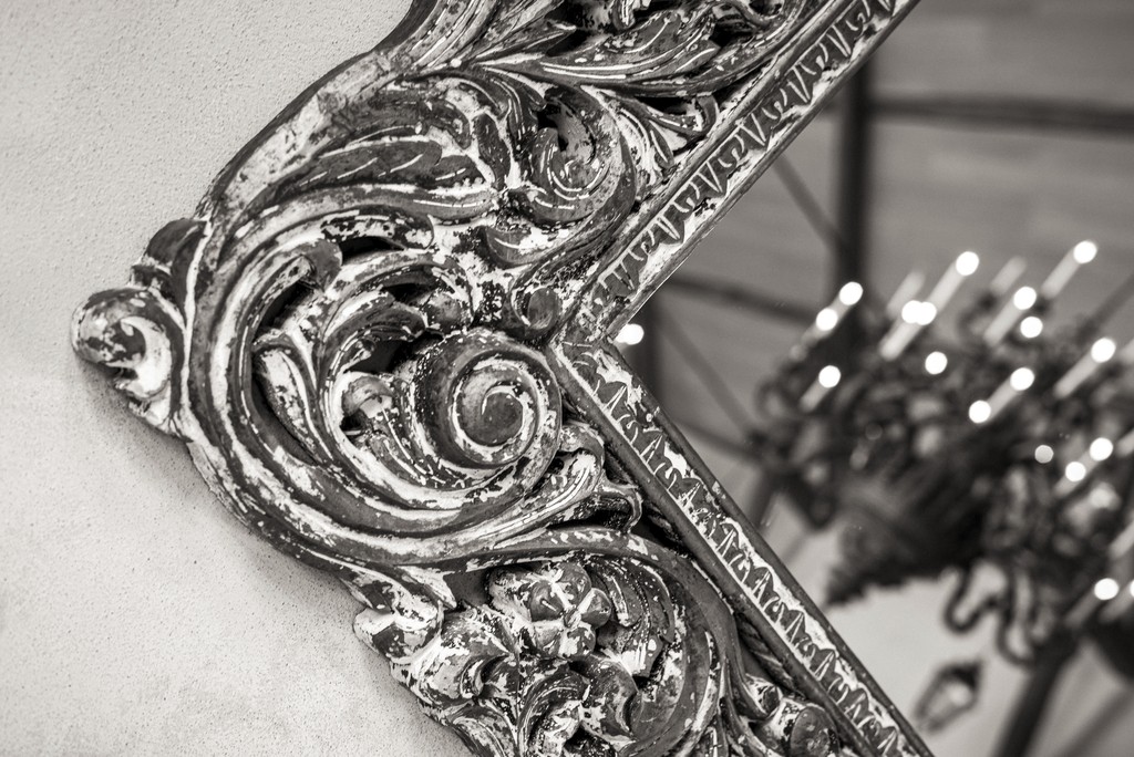 Close-up of an ornate antique mirror frame with golden patina reflecting a chandelier — fine art detail from an elegant wedding venue. Gros plan sur un cadre de miroir ancien orné d’une patine dorée reflétant un lustre — détail artistique d’un lieu de mariage raffiné.