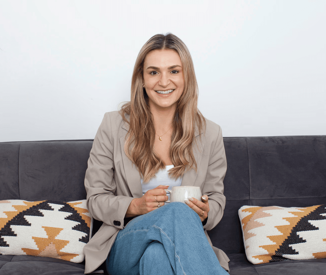 Woman sitting on a sofa holding a mug, smiling in a bright, comfortable living room.