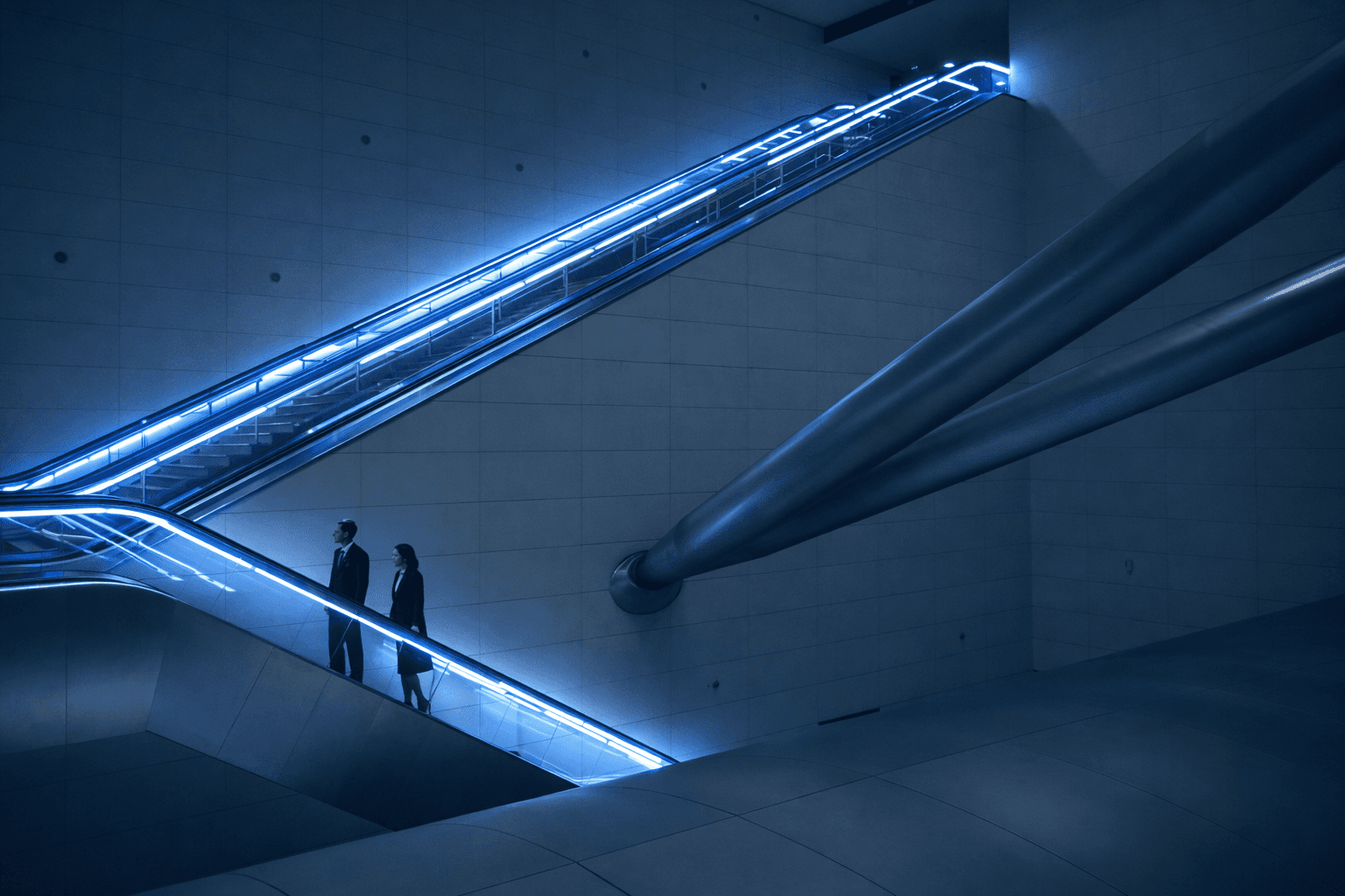 A person with glasses and a beard smiles warmly while working on a laptop at a desk. The setting is casual and relaxed, with a neutral background