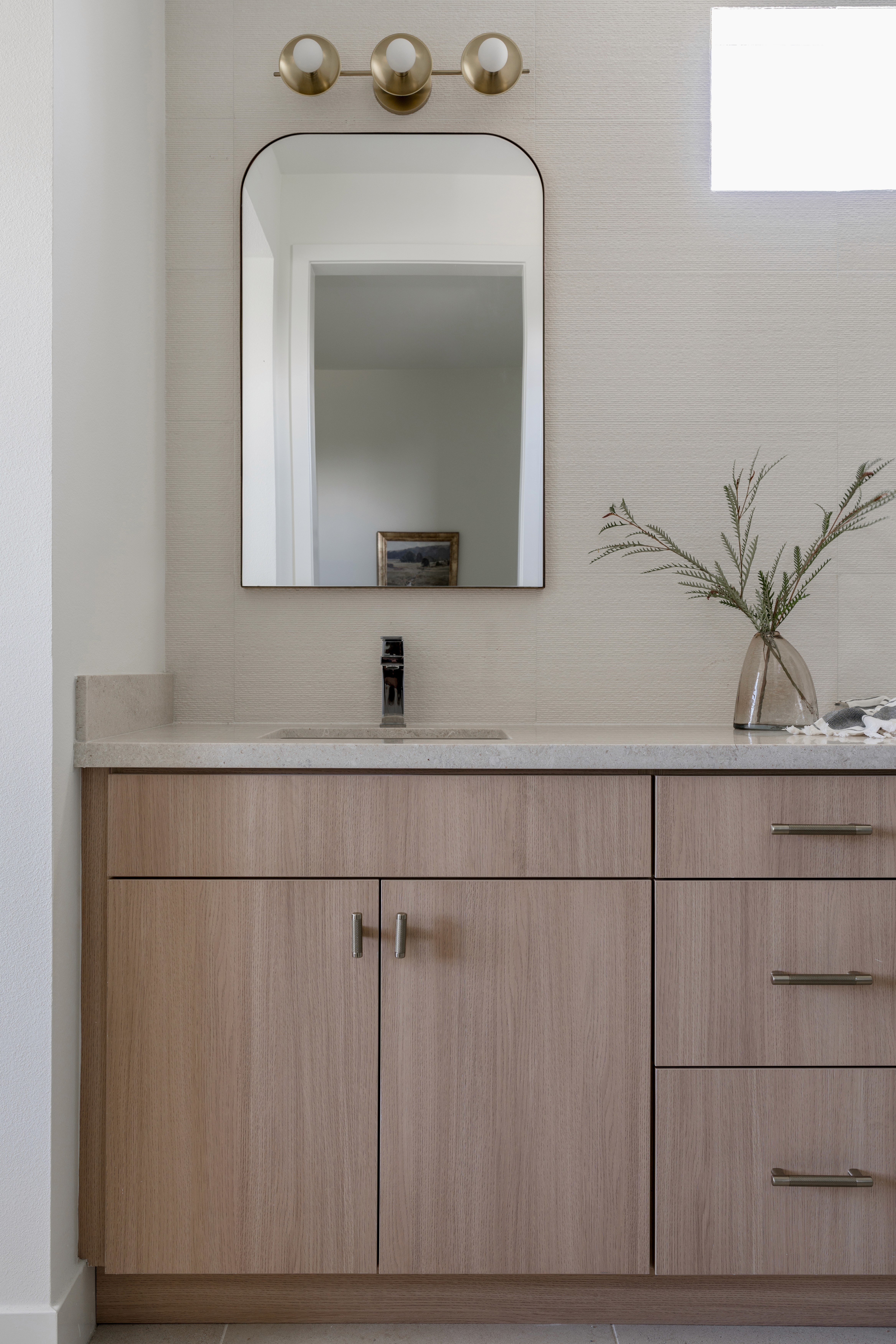 Bathroom vanity with light wood flat paneled cabinetry, off-white countertops, beige walls, rectangular wall mirror, and chrome faucet