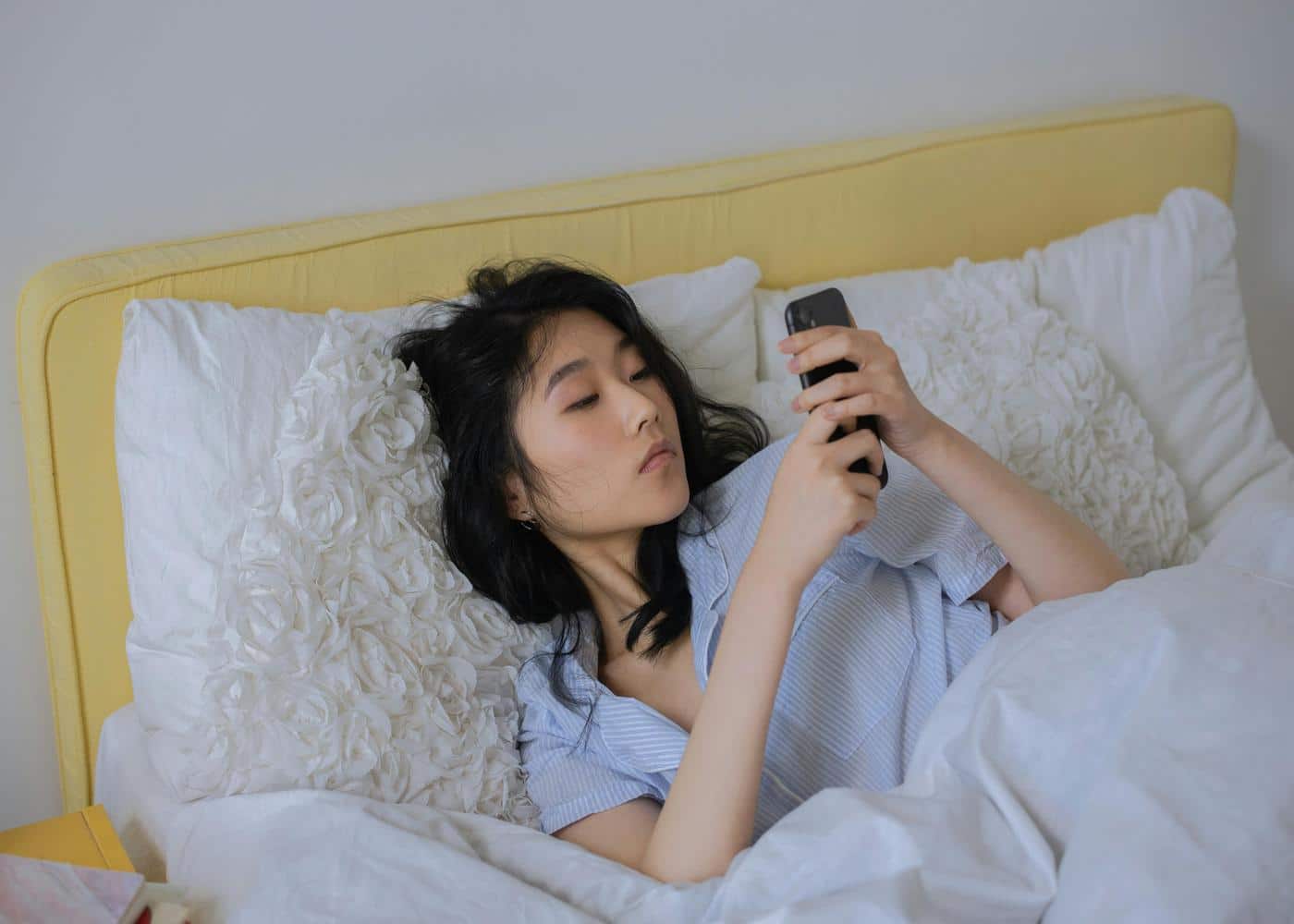 Tired looking woman starting at phone while laying in bed