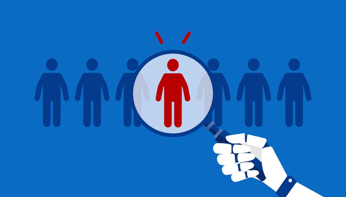 Illustration of a robotic hand holding a magnifying glass over a highlighted red human figure among identical blue figures, symbolizing AI recruitment, candidate detection, and best practices for integrating technology into hiring.