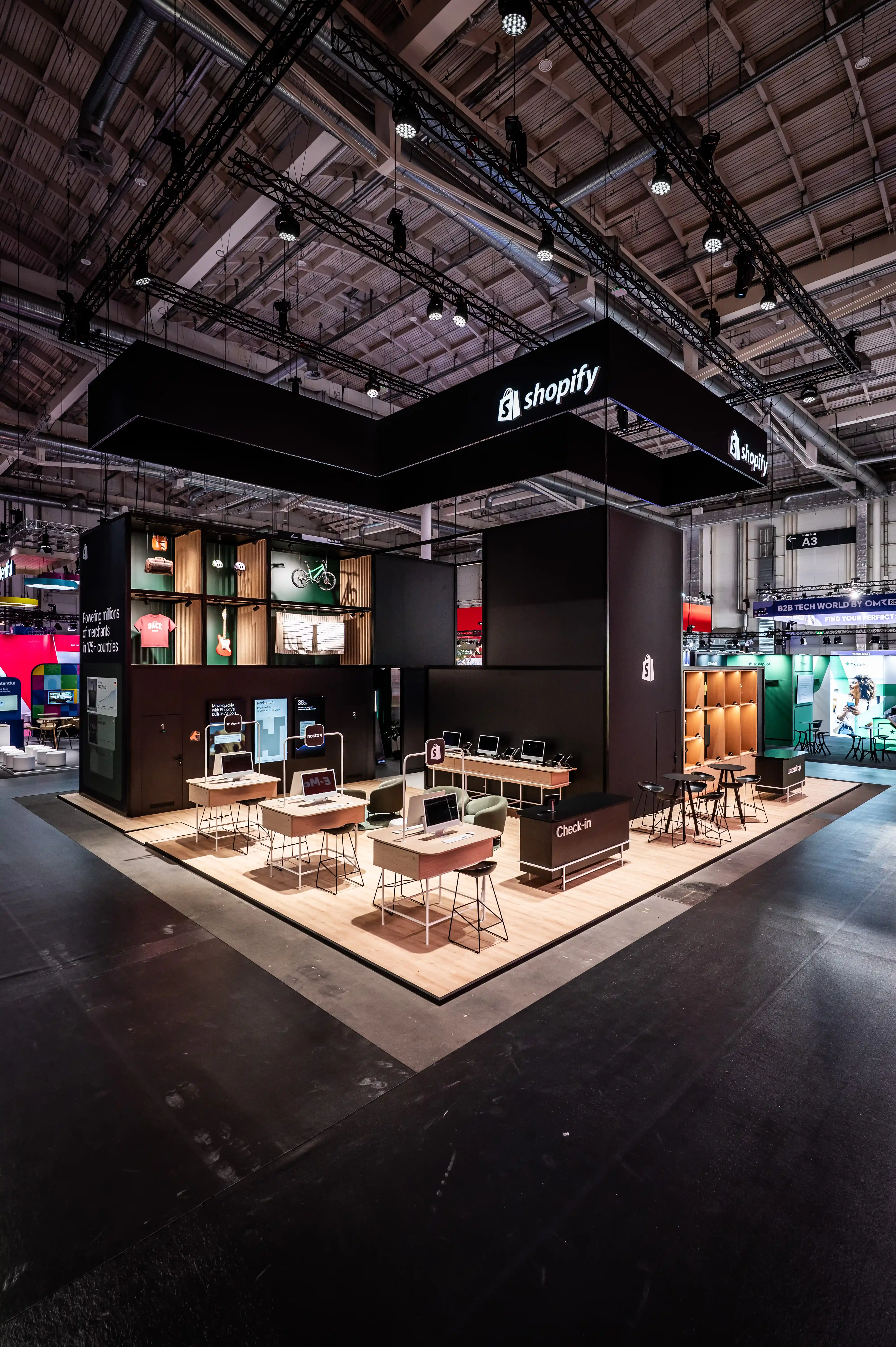 Overview of the Shopify booth with black hanging banner, wooden floor and demo workstations.