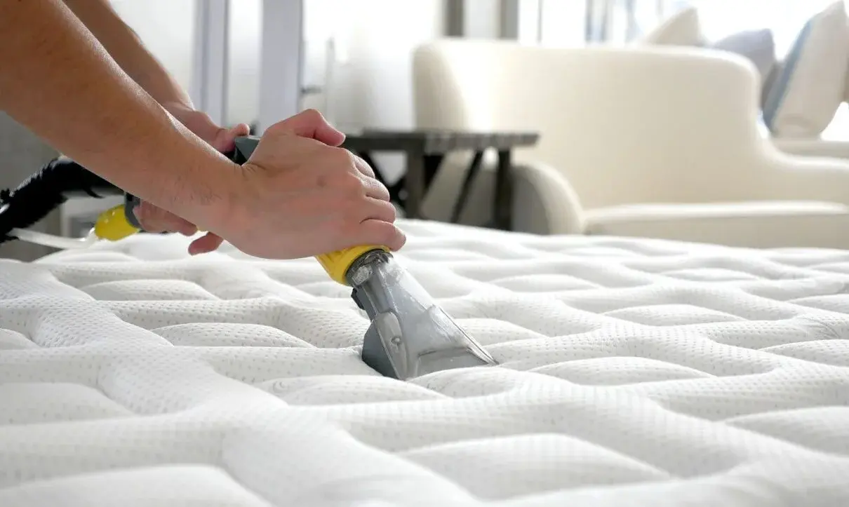 Professional cleaner using vacuum attachment to deep clean white mattress