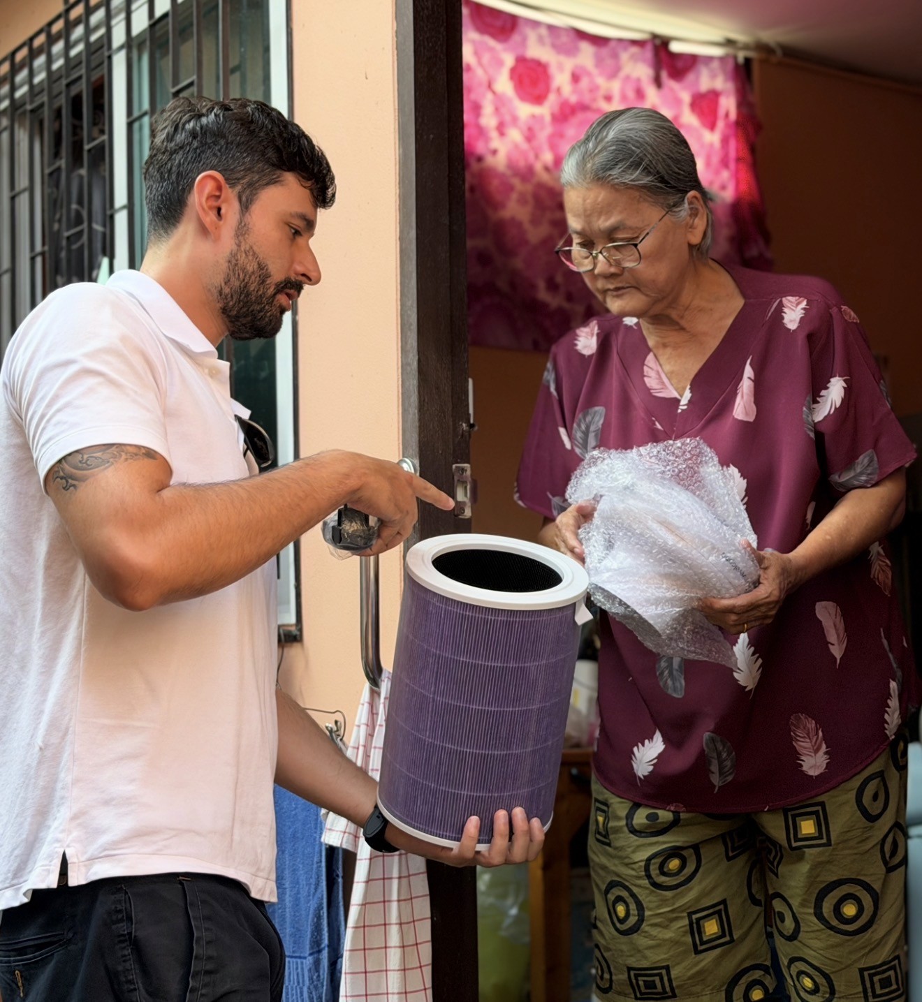 man in blue t-shirt and white floral skirt holding black smartphone while sitting on sidewalk