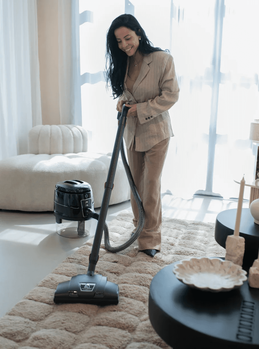 Dunkelhaarige Frau im beigen Anzug reinigt mit dem HYLA System einen flauschigen Teppich im hellen Wohnzimmer