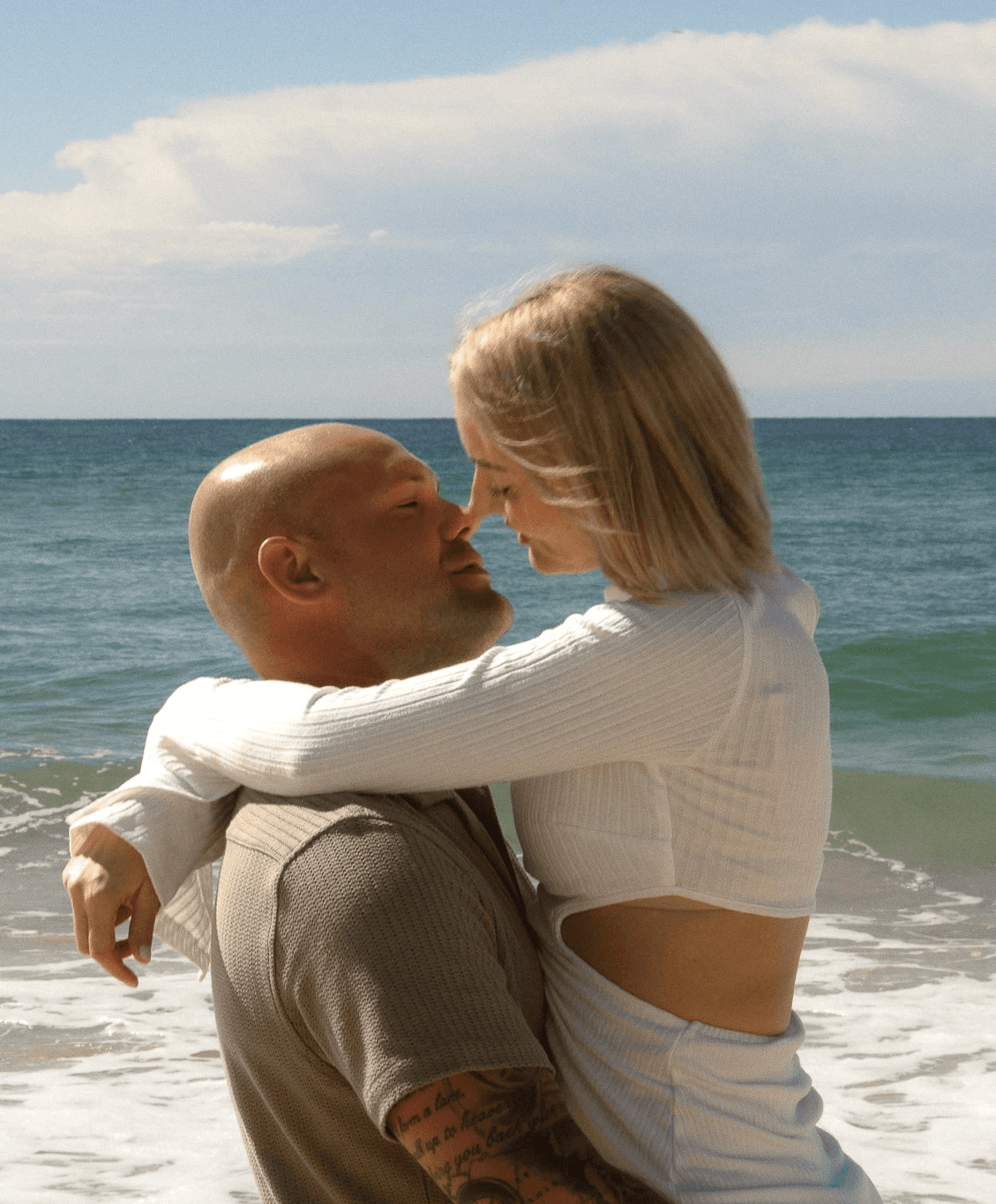 Couple embracing on a sunny beach with the ocean behind them.